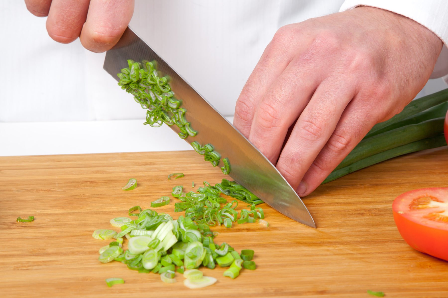 Chef slicing scallions on wooden cutting board