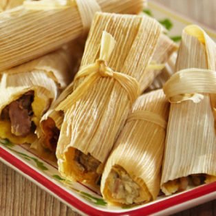 overflowing platter of tamales, wrapped in corn husks