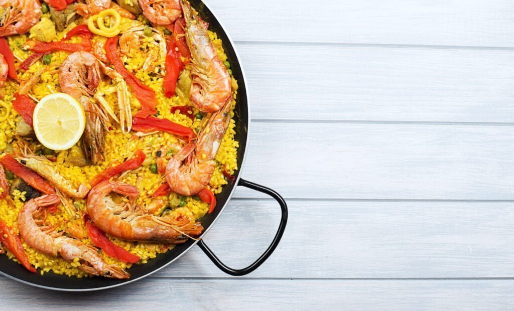 From above paella dish in a pot containing rice and vegetables with seafood.