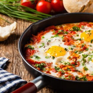 Shakshouka, dish of eggs poached in a sauce of tomatoes, chili peppers, onions. Front view.