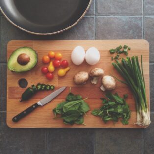 cutting board with green onions, mushrooms, eggs, tomatoes and an avocado