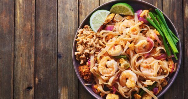 shrimp pad thai on plate in flat lay composition with copy space atop rustic wooden table